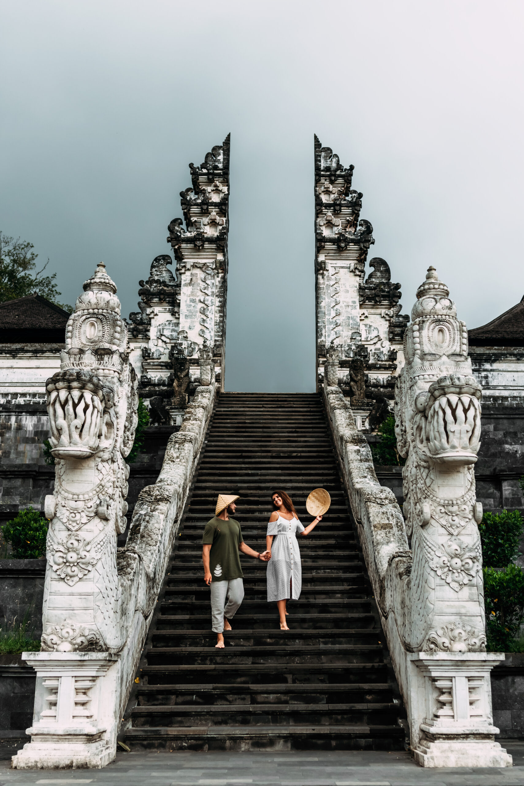 A couple stands on the stairs of the Baltic temple. Man and woman traveling in Indonesia. Couple at the Bali gate. The couple travels the world. Tourists in Bali. Copy space. Vertical photo