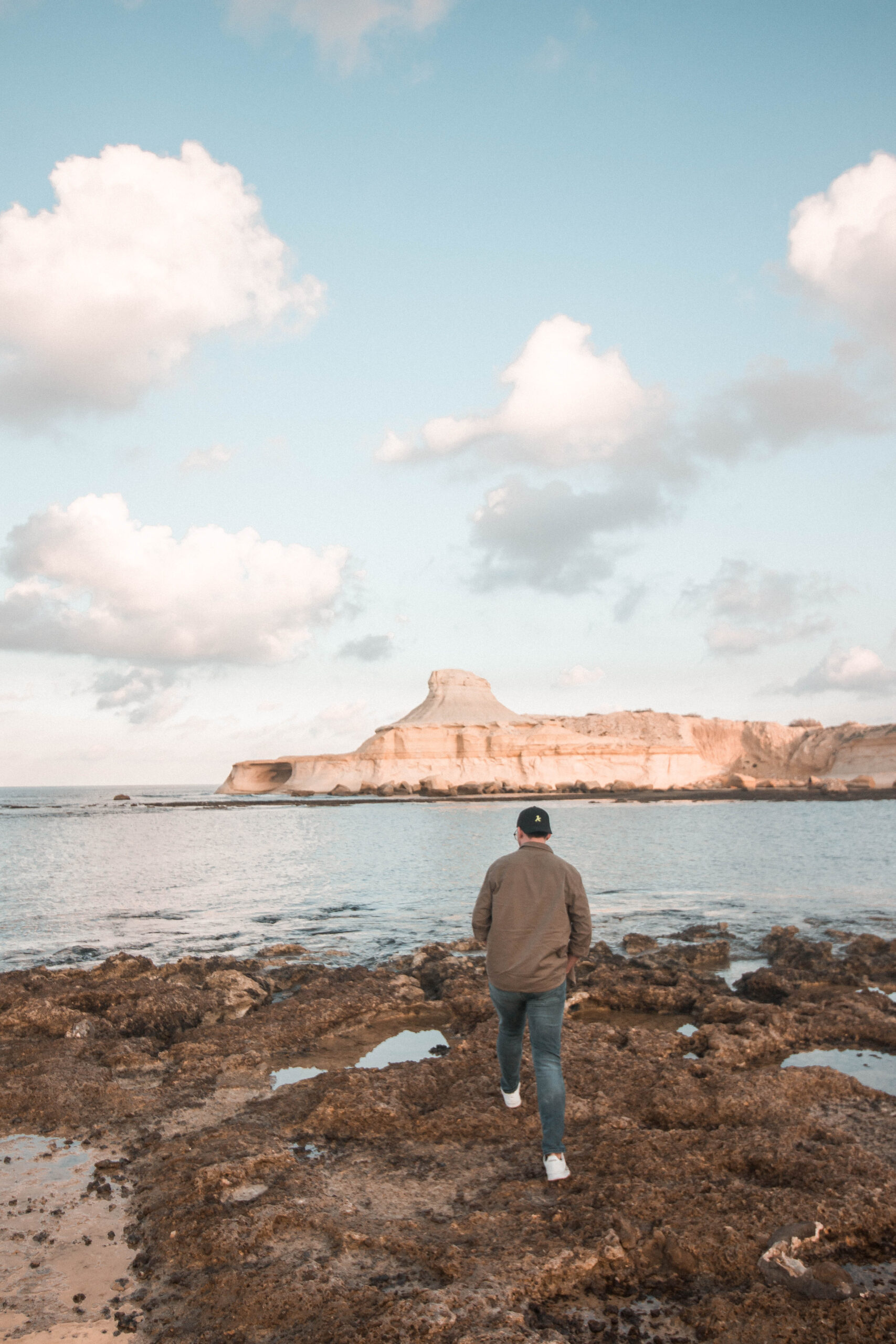 Man strolling on a rocky shore by the ocean under a cloudy blue sky