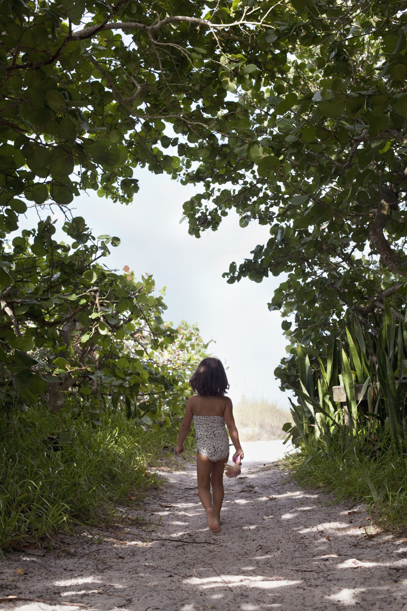 Rear view of girl wearing bathing costume walking along woodland beach path